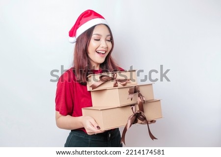 A happy young woman is wearing Santa Claus' hat and holding Christmas presents. 