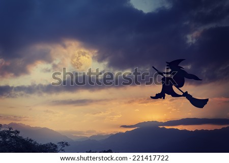 Silhouette of Halloween witch flying on broomstick in the evening under dramatic sky 