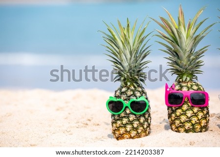 Tropical summer vacation family holiday, Pineapples wearing stylish sunglasses on the sand beach with sea background, Sunny day on the beach tropical island, summer tropical pineapple.