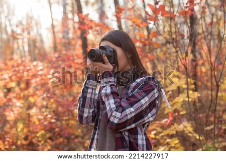Young woman taking photos on DSLR camera in autumn forest