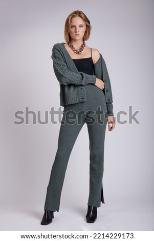 High fashion photo of a beautiful elegant young woman in a pretty green knitwear sweater, pants, trousers black top posing over white, soft gray background. Studio Shot, portrait. 