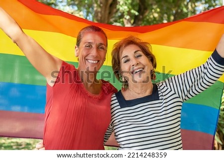 A middle-aged girl next to an older lady raising the gay rainbow flag. Support for the lgbti+, gay, homosexual, bisexual, lesbian, trans, non-binary community. Fight for the freedom and rights  Royalty-Free Stock Photo #2214248359