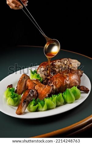 Vertical picture of a crispy roasted Chinese duck. The sauce is poured over. The duck is served on a white place with steamed green vegetables. The duck is stuffed.