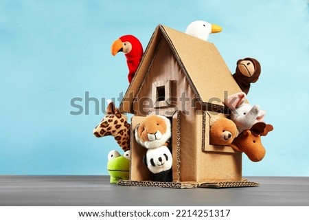 Ten animal finger puppets coming out of a cardboard craft house on a blue background