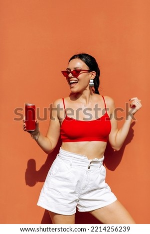 A girl on an orange background with a red tin can in her hands. Cheerful girl, advertising shooting. High quality photo Royalty-Free Stock Photo #2214256239