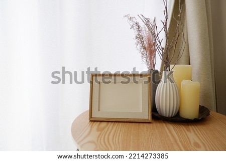 White and gray vase on a natural brown wooden table with white dried flowers, candles, clock and blank photo frame in a room. autumn and winter interior image photo.