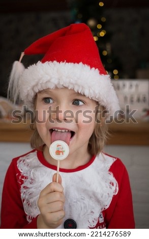 cute boy in red santa hat licks sweet holiday lollipop. sweet holiday Christmas, New Year, Festive mood. santa's little helper