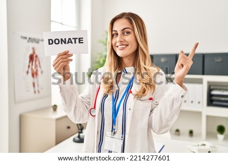 Young blonde doctor woman supporting organs donations smiling happy pointing with hand and finger to the side 