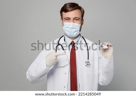 Male doctor man wears white medical gown suit mask gloves work in hospital hold in hand thermometer show temperature isolated on plain grey color background studio portrait Healthcare medicine concept
