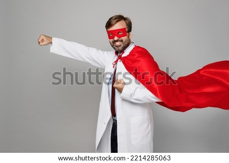 Side view male doctor man wear white medical gown suit work in hospital wear red super hero coat stand akimbo hands on waist isolated on plain grey color background studio. Healthcare medicine concept