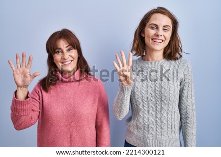 Mother and daughter standing over blue background showing and pointing up with fingers number nine while smiling confident and happy. 