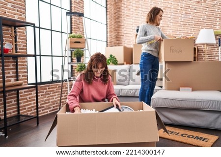 Two women mother and daughter unpacking cardboard box at new home Royalty-Free Stock Photo #2214300147