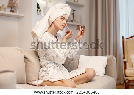 Woman wearing dressing gown and has a towel on her hair doing a make up Royalty-Free Stock Photo #2214305407