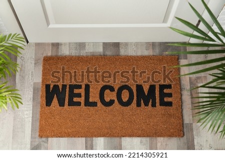 Door mat with word Welcome on wooden floor in hall, top view Royalty-Free Stock Photo #2214305921