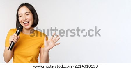 Happy asian girl dancing and singing karaoke, holding microphone in hand, having fun, standing over white background Royalty-Free Stock Photo #2214310153