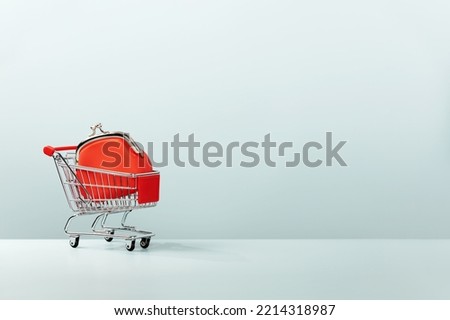 Metallic shopping cart trolley and Red Coin Purse on blue background with copy space. Shopping symbol