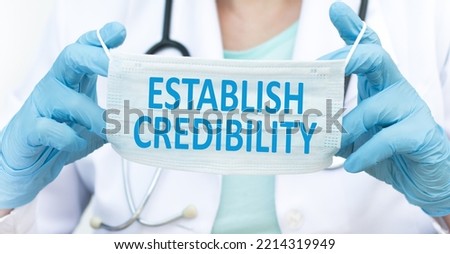 ESTABLISH CREDIBILITY text on a protective mask in the hands of a doctor, medical concept