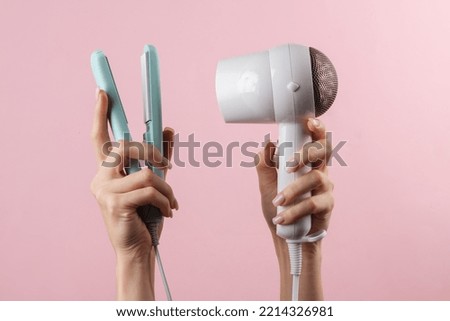 Fashionable modern hair dryer and hair straightener in female hands on a pink background. Hair style Royalty-Free Stock Photo #2214326981