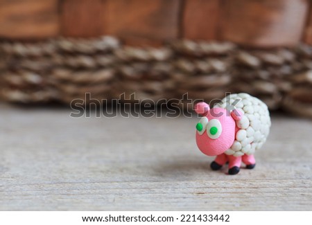 Plasticine world - little homemade white sheep with green eyes stand on a wooden floor, selective focus and place for text