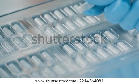 Pharmacologist checks blister packs with medicinal capsules moving on a conveyor. Plastic package with capsule meds. Medication capsules in blisters. Pharmaceutical factory production line. Macro Royalty-Free Stock Photo #2214364081