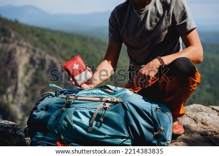 A person holds in his hand a first-aid kit, tourist equipment, a hiking backpack, a red first-aid kit in the mountains, a collection of equipment. High quality photo