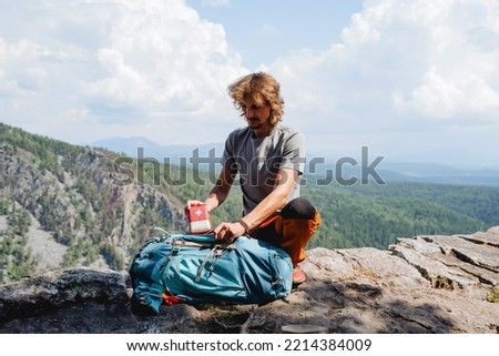 Take the first aid kit out of the backpack, the guy puts a first aid kit in the backpack, a tourist in the mountains collects equipment, a man on top of a mountain. High quality photo