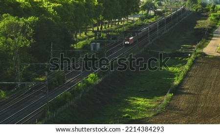 Aerial view of fast passenger train driving on railroad. High angle view of passing high speed train in rural summer country landscape. Train movement aerial view, parallax effect. Royalty-Free Stock Photo #2214384293