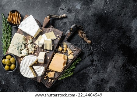 Delicious Cheese board. Assortment of cheese, camembert, brie, Gorgonzola, parmesan, olives, nuts and herbs. Black background. Top view. Copy space. Royalty-Free Stock Photo #2214404549