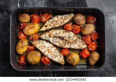 Roasted halibut fish steaks with tomato and potato. Black background. Top view.