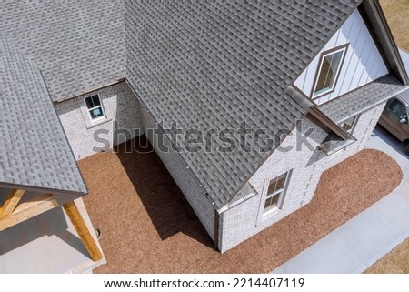 Roof of newly built house is being covered with asphalt shingles during construction while house is still being built Royalty-Free Stock Photo #2214407119
