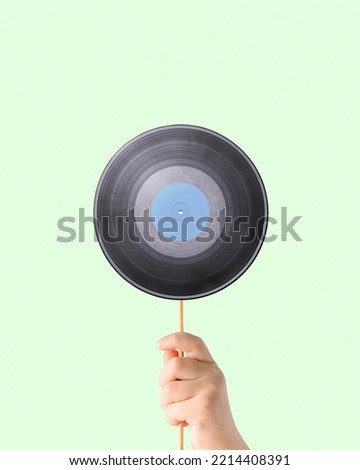 Minimal creative, abstract, music retro concept made with child’s hand holding stick with gramophone record on isolated, light, pastel green background. Musical party idea.