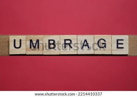 text the word umbrage from gray wooden small letters with black font on an red table Royalty-Free Stock Photo #2214410337