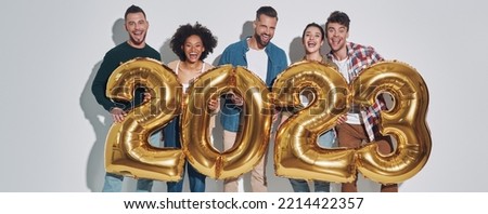 Group of young beautiful people in casual clothing carrying gold colored numbers and smiling