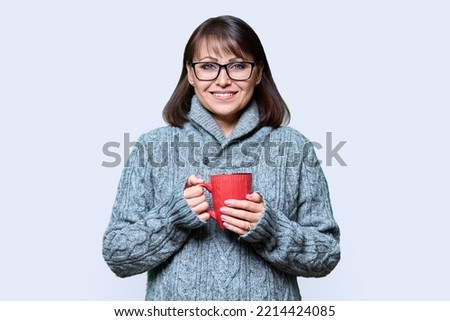 Winter portrait of happy woman in sweater with mug on light background