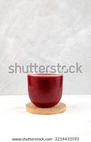 Red fruit  berry smoothie in clear glass on grey background. Refreshing healthy cocktail, antioxidant slush drink.