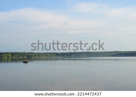 Fisherman in a boat is fishing on lake in early morning. Beautiful lake or river landscape with a fisherman