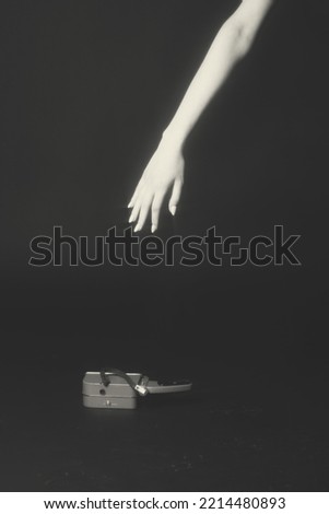 Composition of slim and skinny bright woman hand reaching old retro video camera. Metallic camera is on dirty studio black background. Glowing hand due to star filter. Toned image with yellow color
