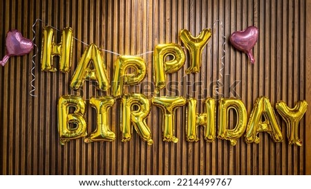 "Happy Birthday" golden balloon texts which is aligned on wooden wall for decorate the party event. Object and background photo.
