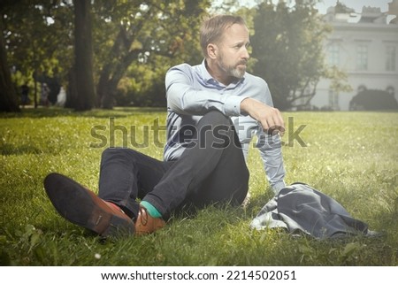 Man in blue suit with shirt and tie sitting on grass in summer park