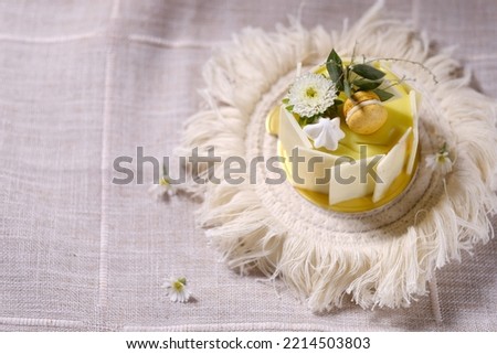white small cake decorated with white ester flowers, and leaves on a textured cloth background.
