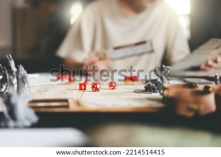 Role playing tabletop and board games hobby concept. Focus on dice d20. Blur background with people and monster miniatures. Royalty-Free Stock Photo #2214514415
