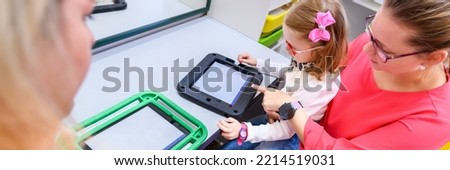 Non-verbal girl living with cerebral palsy, learning to use digital tablet device to communicate. People who have difficulty developing language or using speech use speech-generating devices. Royalty-Free Stock Photo #2214519031