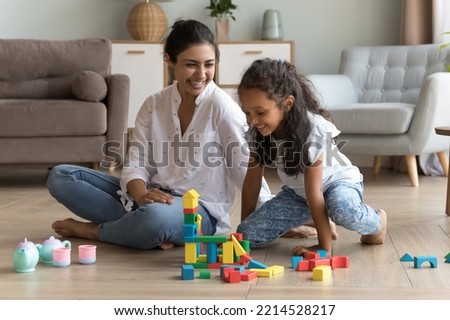 Indian woman and daughter play wooden blocks seated on floor smiling looking happy, enjoy carefree weekend leisure and pastime, having fun together at modern living room. Playtime at home with child Royalty-Free Stock Photo #2214528217