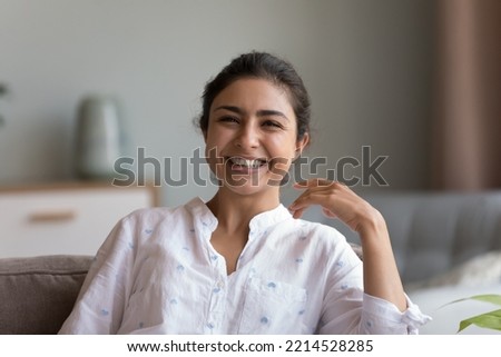 Head shot young Indian woman sit on couch smile look at camera. Happy female rest on comfortable sofa at home laughing enjoy carefree leisure at new modern apartment. Tenant portrait, positive emotion Royalty-Free Stock Photo #2214528285