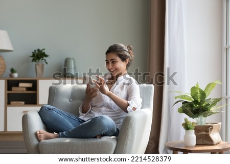 Happy Indian woman resting on cozy chair with smarthome, share messages to friend in social networks smile enjoy free time on internet. E-dating apps services for singles, electronic shopping at home Royalty-Free Stock Photo #2214528379