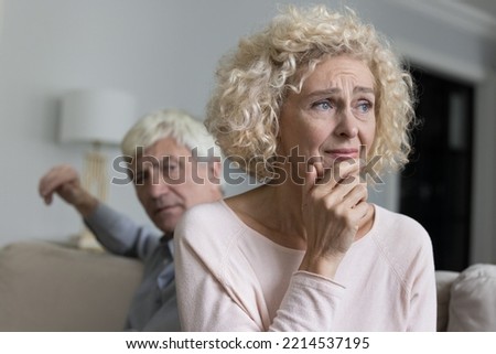 Close up shot of sad disappointed unhappy older woman suffers from misunderstanding or resentment sit on sofa with frown angry husband after quarrel. Break up, divorce, emotional abuse, bad relations Royalty-Free Stock Photo #2214537195