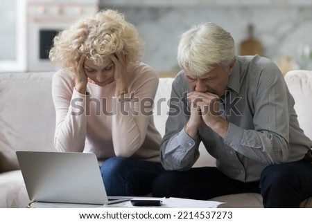 Upset frustrated senior couple sit on sofa at table with heap of bills feel desperate due to lack of money to pay monthly utility, high rates, unpaid taxes, bank notice about eviction of older debtors Royalty-Free Stock Photo #2214537273
