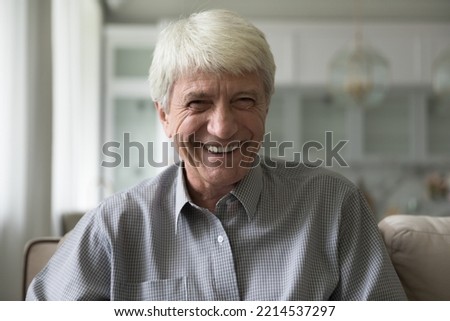 Happy senior take part in video call smile looks at cam, laughing, enjoy remote talk participate in videoconference to family living abroad. Virtual meeting event profile picture of old man, head shot Royalty-Free Stock Photo #2214537297