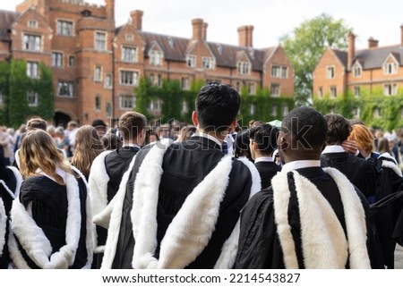 back view of Male and female fresh graduate international British Black African students with gown and academic address walk in campus Selwyn College, Cambridge University, UK on congregation day. Royalty-Free Stock Photo #2214543827