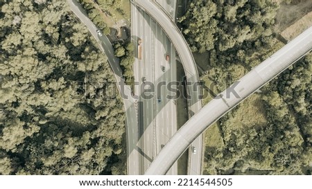 Aerial view directly above a six lane highway. Top view of asphalt road passes through the field and forest. Aerial. Sedan cars driving by the highway. Top view from drone. aerial photo autobahn road Royalty-Free Stock Photo #2214544505